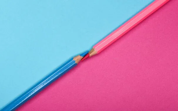 Two coloured pencils meeting tip to tip against a split pink and blue background
