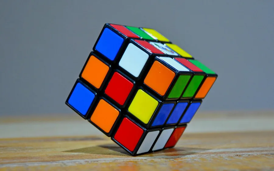 A colourful Rubik's cube resting at an angle on a wooden surface